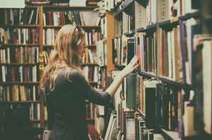 woman in black long sleeved looking for books in library